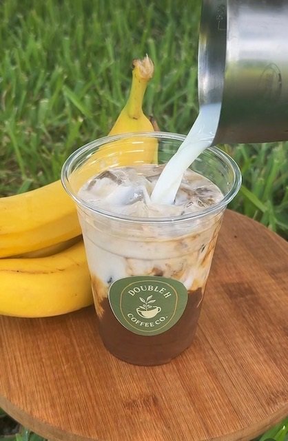 Iced coffee on a wooden table next to fresh bananas at the Double H Coffee Co. trailer
